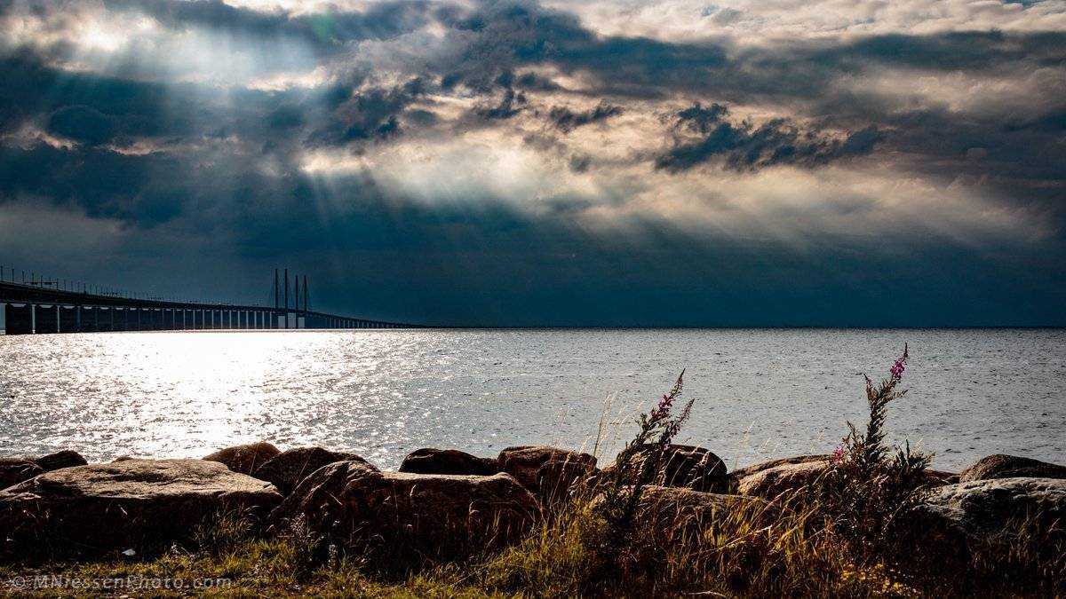 1st Place Michael Niessen @MNiessenPhoto Sun rays slashing through the clouds above the Oresund bridge between Sweden and Denmark.